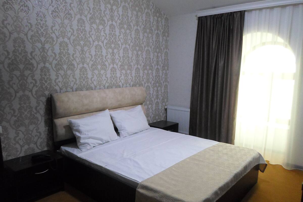 A hotel room with a bed, a nightstand, a dresser, and a window with curtains.
