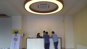 A reception desk with three people standing behind it, a large illuminated ceiling feature, and a promotional stand to the left. - Abu Turan Hotel (Baku)
