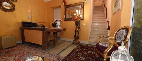 Uma sala de estar com mesa de centro de madeira, poltrona vermelha, mesa lateral branca com luminária, espelho e escada para um andar superior.