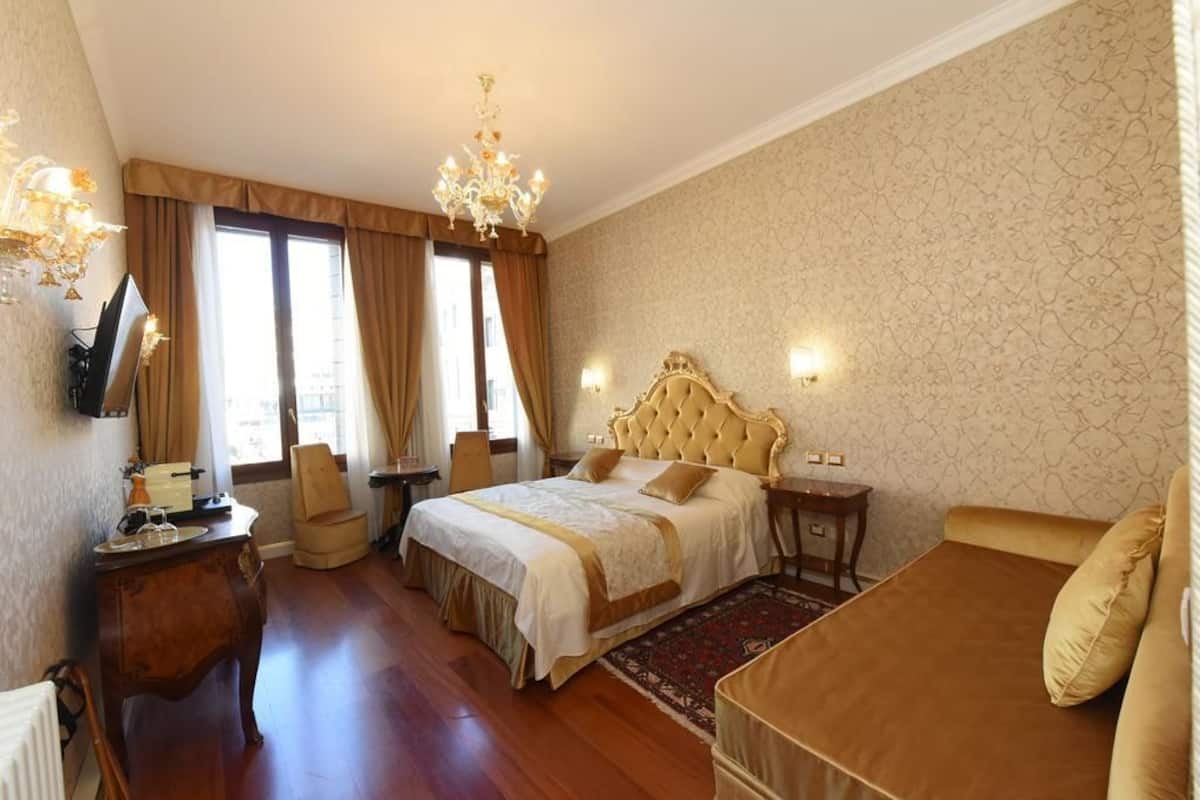 A hotel room with a large bed, a desk with a chair, a television, and a chandelier.