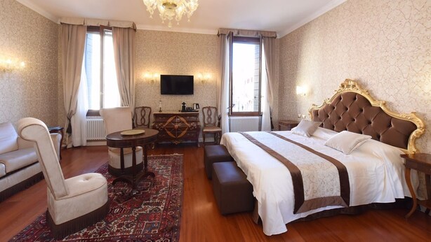 A hotel room with a large bed, a sofa, a small table, a TV, and a chandelier. - 40.17 San Marco (Venice)