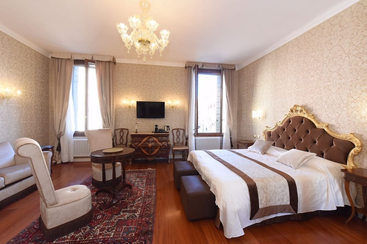 A hotel room with a large bed, a sofa, a small table, a TV, and a chandelier.