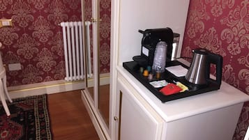 A small kitchenette with a coffee maker, kettle, and tea pot on a counter.