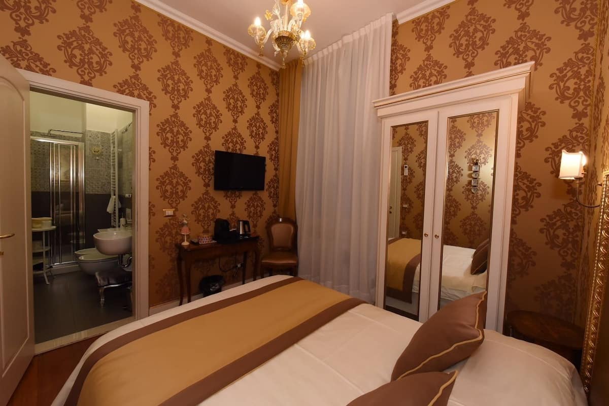 A hotel room with a large bed, a desk with a chair, a television, and a bathroom visible through an open door.