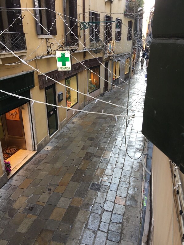 A narrow street with a pharmacy sign, stone pavement, and buildings with barred windows.