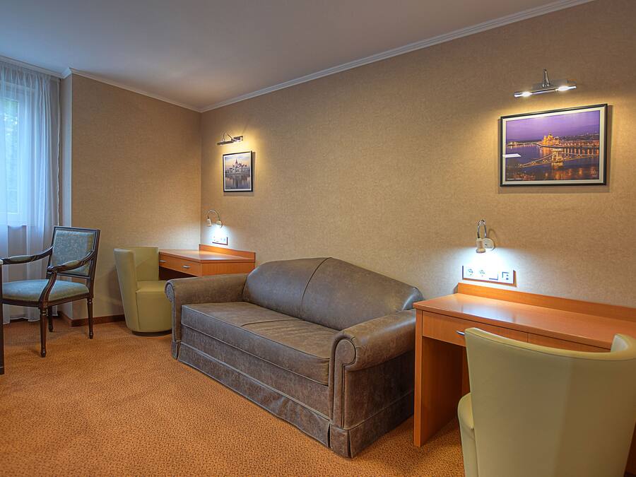Habitación de hotel con sofá, dos sillones, escritorio y una silla. Hay dos lámparas de pared y dos cuadros enmarcados.