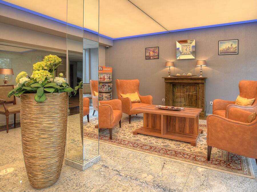 A lobby with a reception desk, two sofas, a coffee table, a large vase with flowers, and a wooden cabinet.