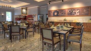 Restaurante com chão de mármore, cadeiras e mesas de madeira preparadas para refeições.