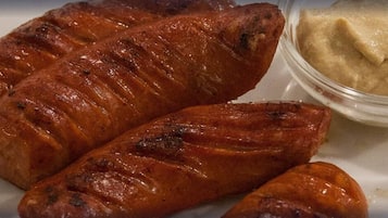 Tres salchichas a la parrilla y un recipiente pequeño de mostaza sobre un plato blanco.