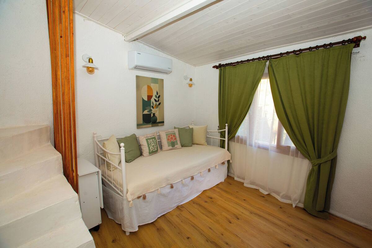 A bedroom with a bed, a nightstand, a painting, and a staircase.