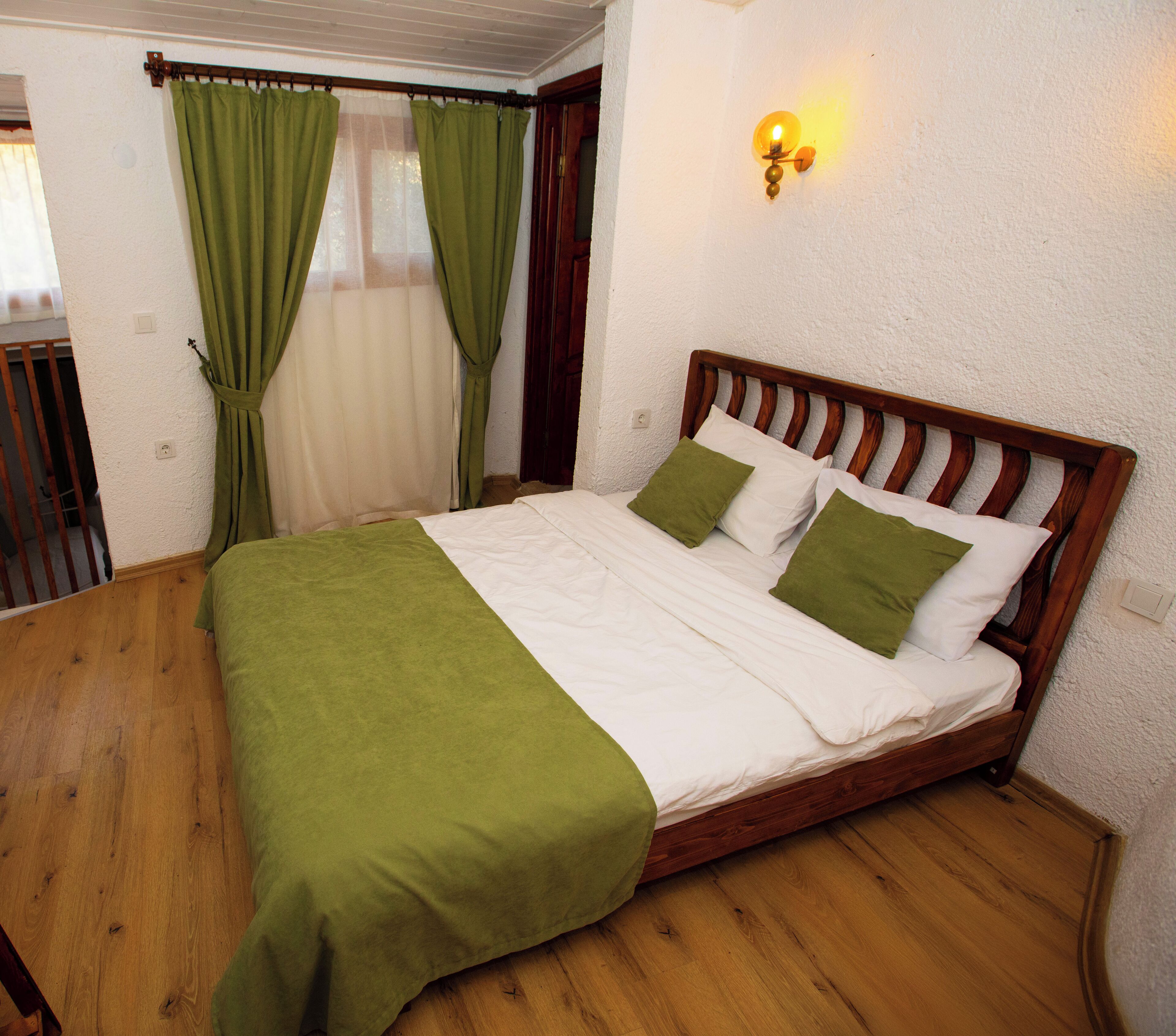 A bed with a wooden headboard, green bedding, and a wall-mounted light fixture.
