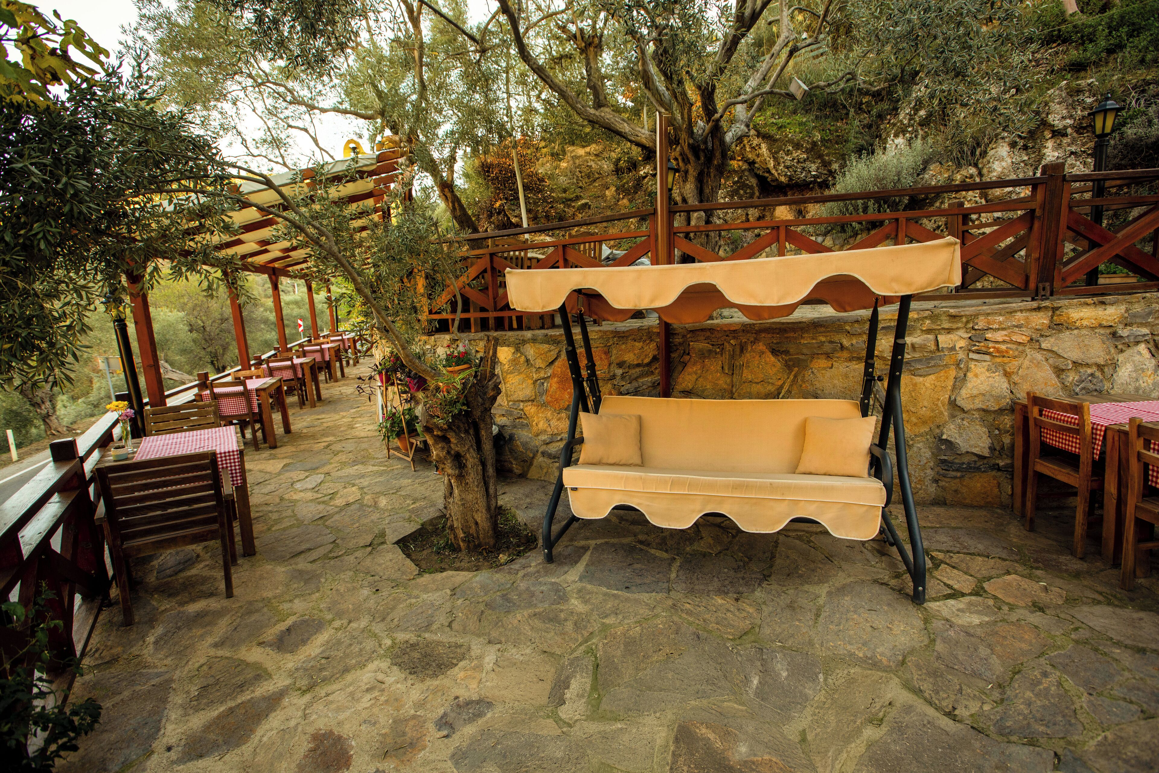 An outdoor seating area with stone flooring, wooden tables and chairs, and a swing chair.