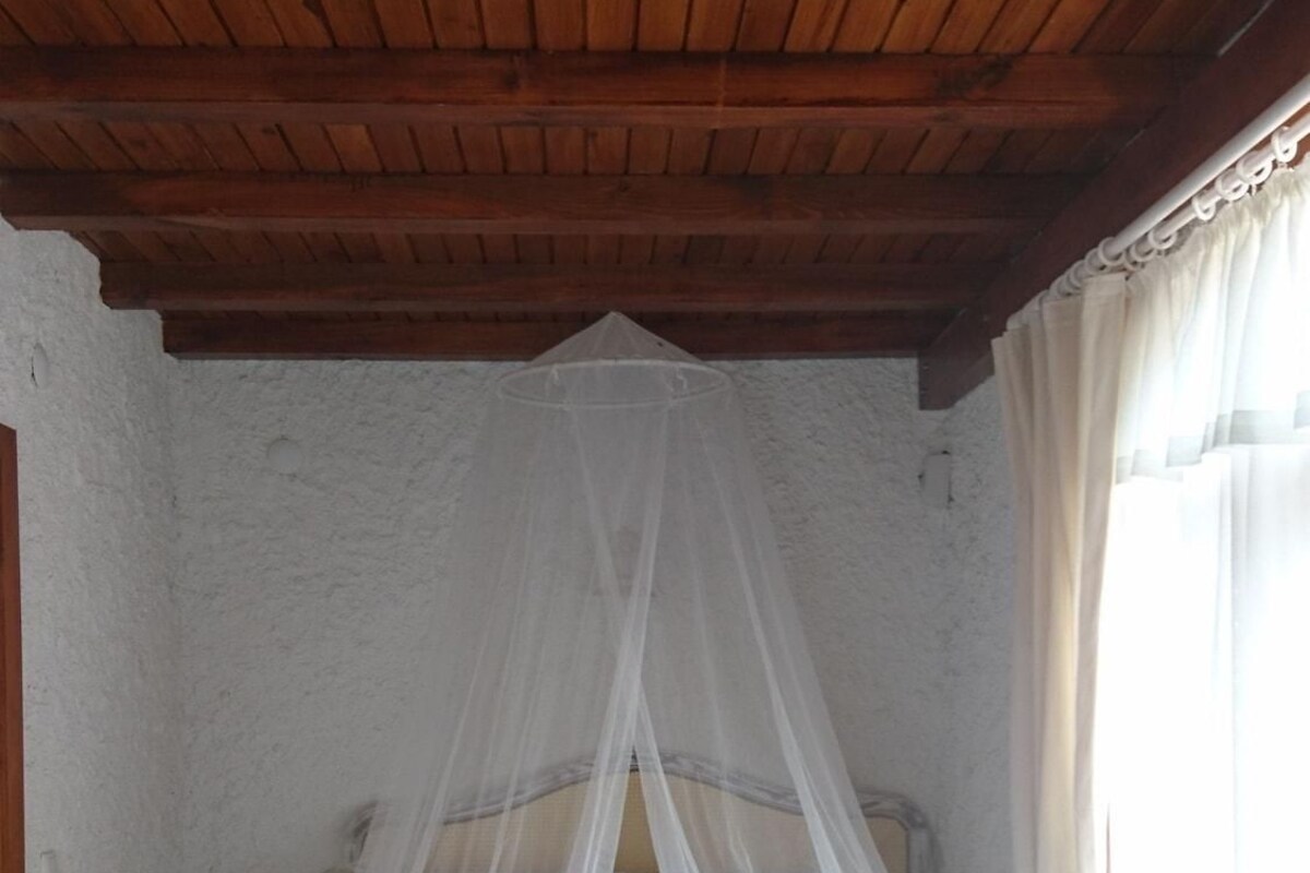 Ein Bett mit Baldachin, eine weiße Wand und eine Holzbalkendecke.