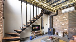 Una sala de estar moderna con una escalera de madera, un televisor, una chimenea y una pared de ladrillo rústico.