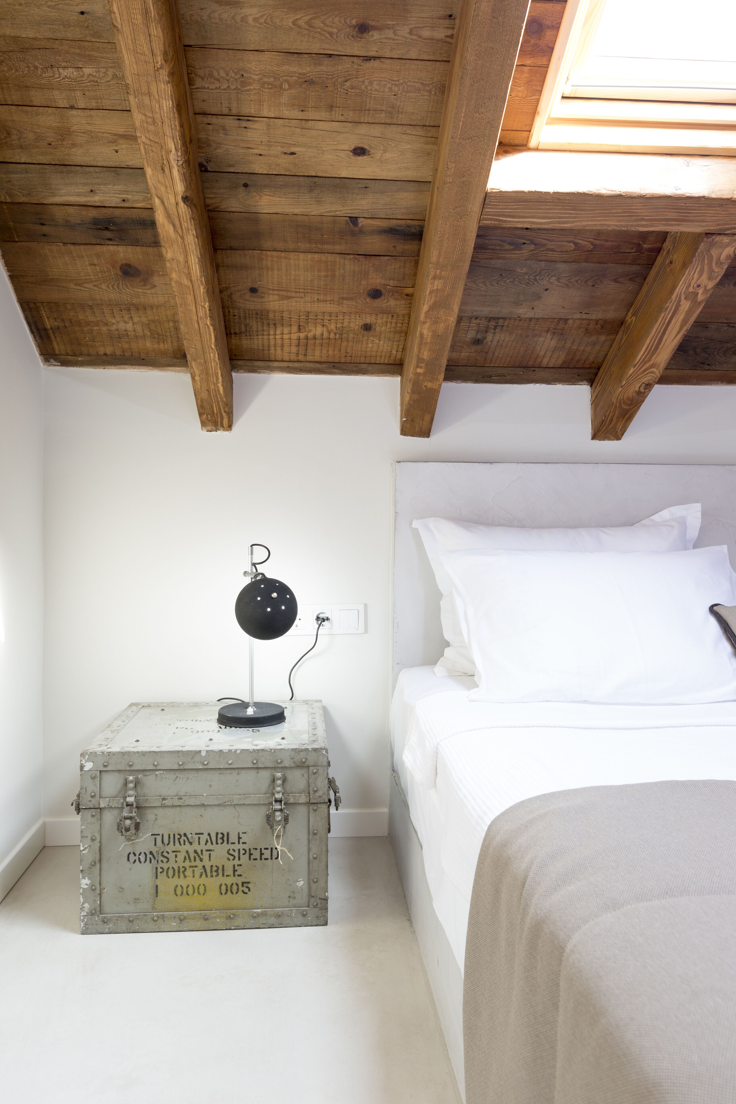 Ein Schlafzimmer mit Holzboden, einem Bett mit weißer Bettwäsche und einem Vintage-Koffer mit Aufschrift.