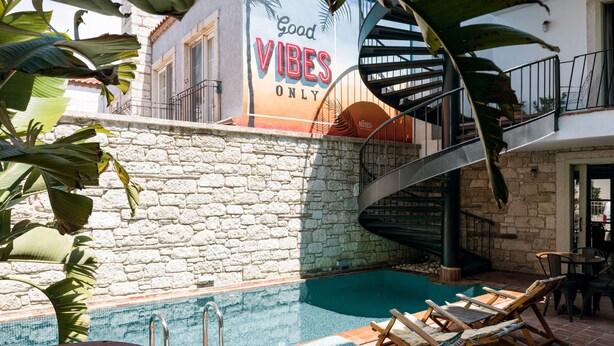 Un área de piscina con sillones de descanso, un muro de piedra y un cartel que dice 'Good Vibes Only'.