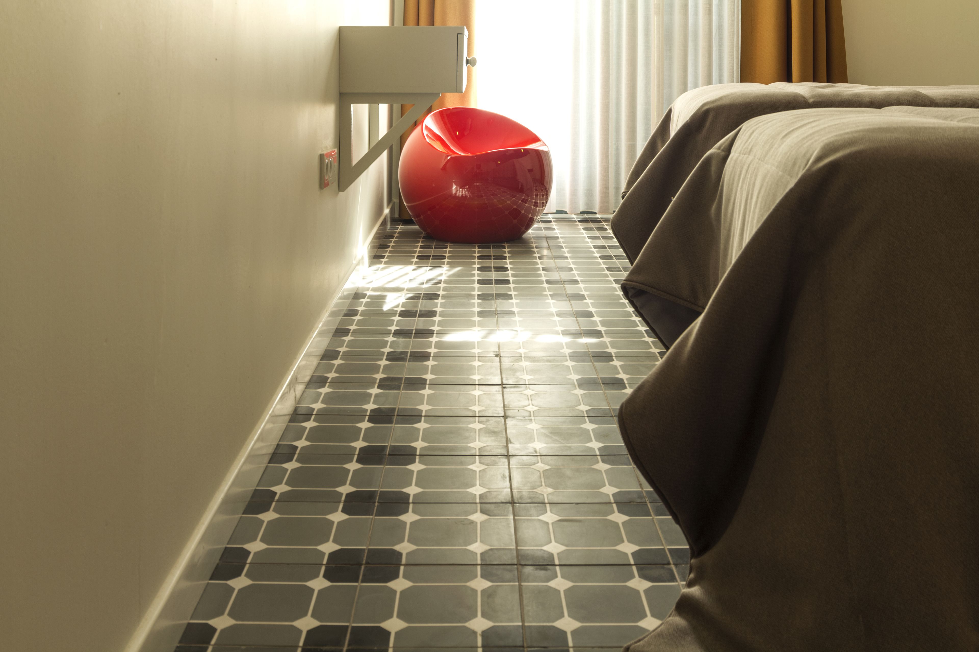 A hotel room with a tiled floor, a red chair, and two beds with brown covers.