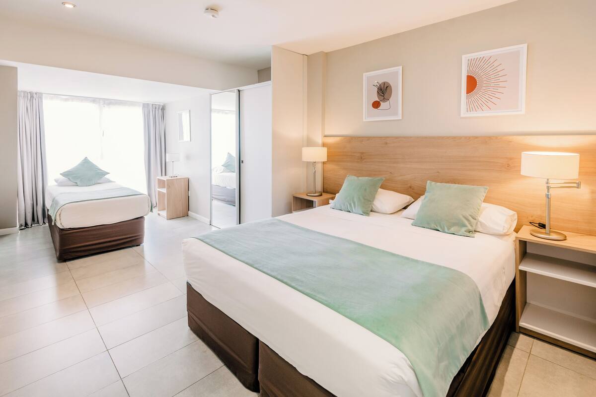 A modern hotel room with a large bed, a separate seating area, and a view through a glass door.