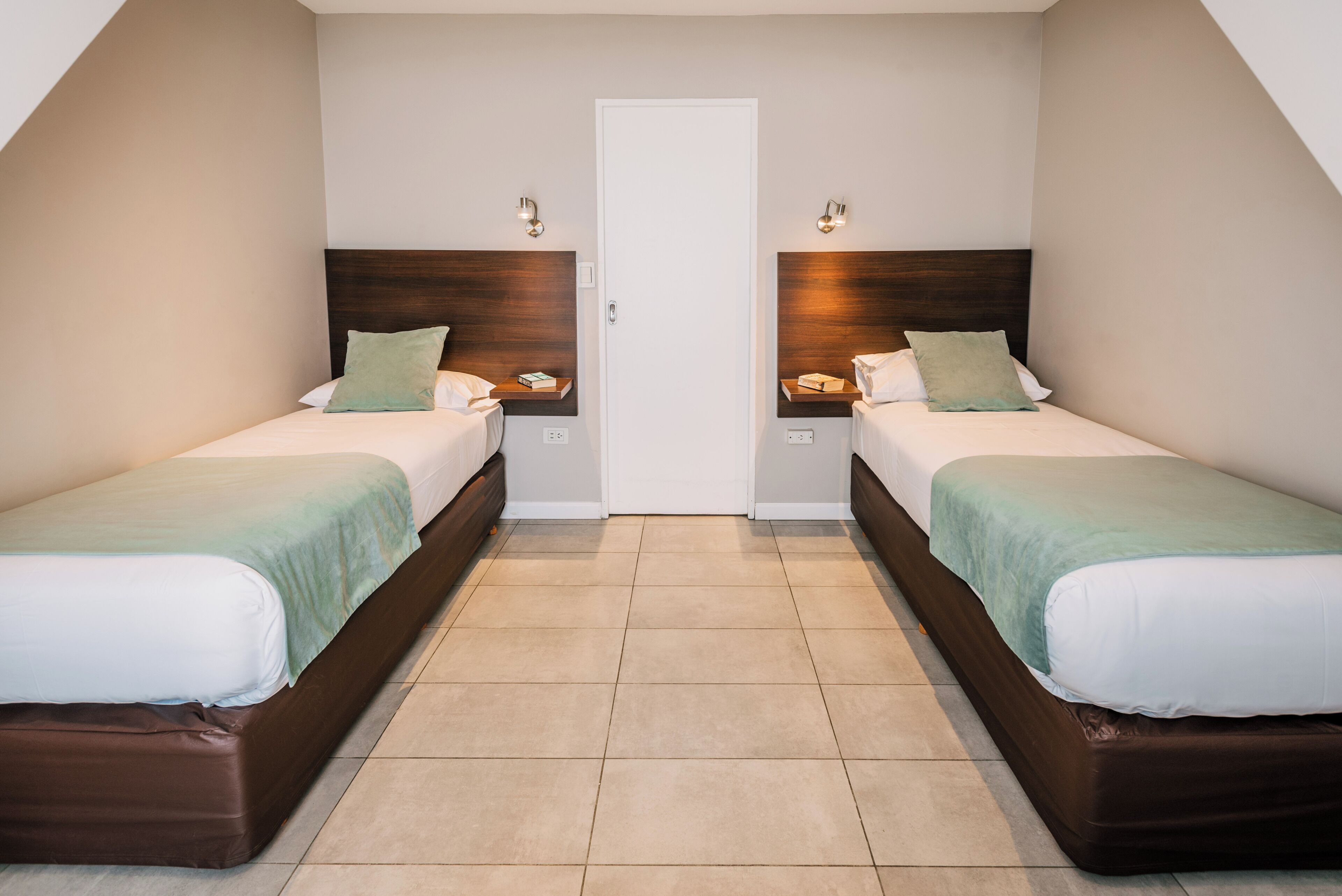 Una habitación con dos camas, una puerta y suelo de baldosas.
