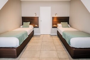 Una habitación con dos camas, una puerta y suelo de baldosas.