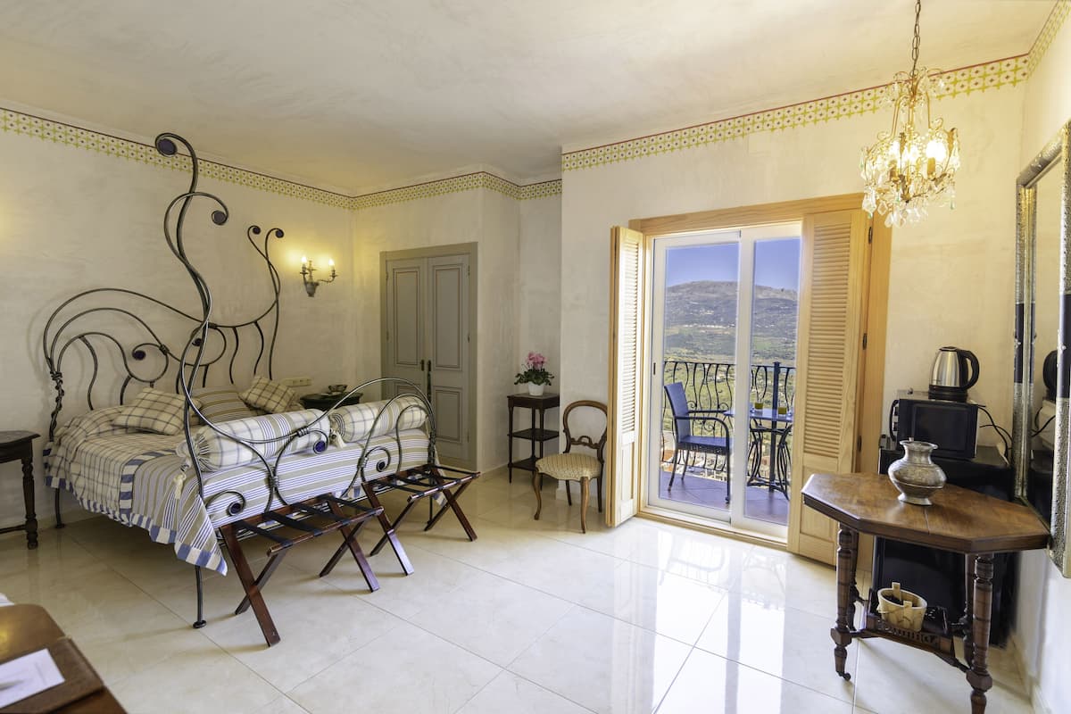 Ein Schlafzimmer mit Bett, Sessel, Tisch, Spiegel und einem Balkon mit Blick.