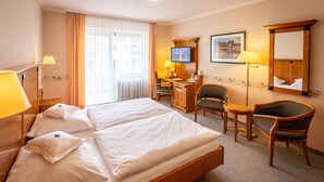Une chambre d’hôtel avec un grand lit, deux fauteuils, un bureau, une télévision et un miroir.