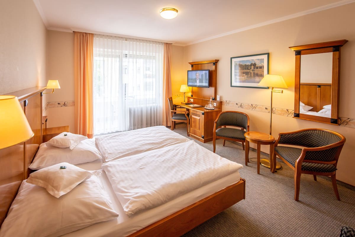 Ein Hotelzimmer mit einem großen Bett, zwei Sesseln, einem Schreibtisch, einem Fernseher und einem Spiegel.