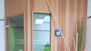 Un sauna avec des murs en bois, une porte en verre, un banc en bois, une petite plante et un bâton en bambou.