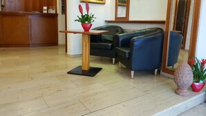 Un espace d’accueil avec un bureau en bois, des fauteuils en cuir noir et une plante en pot.