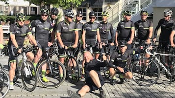 Een groep fietsers in dezelfde outfits die voor een foto poseren op een geplaveid straat.