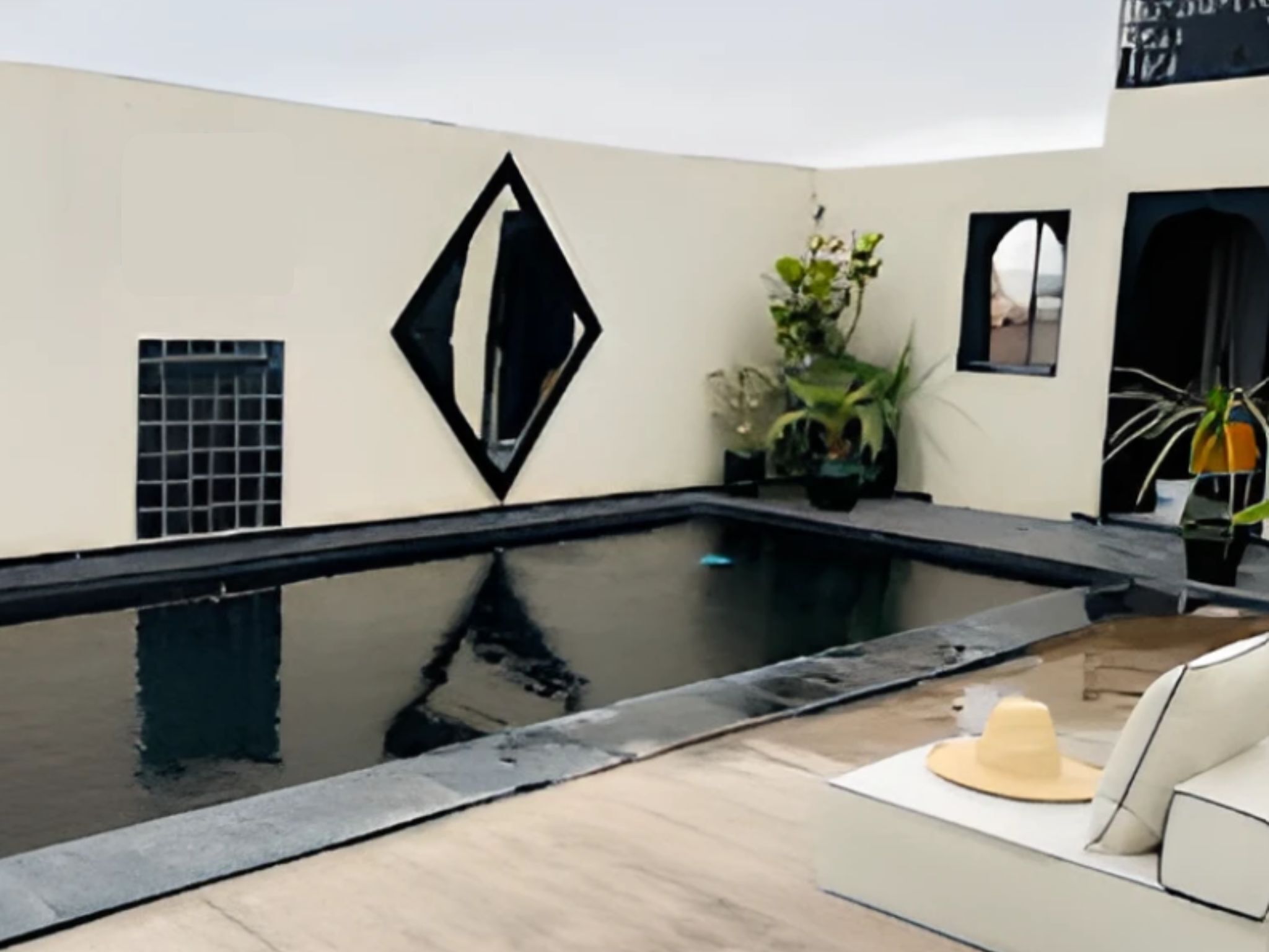 A modern pool area with a geometric wall design, a seating area with a hat, and potted plants.