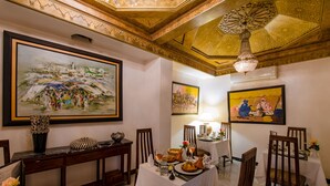 Comedor con mesas dispuestas para una comida, adornado con obras de arte en las paredes y una lámpara de araña.