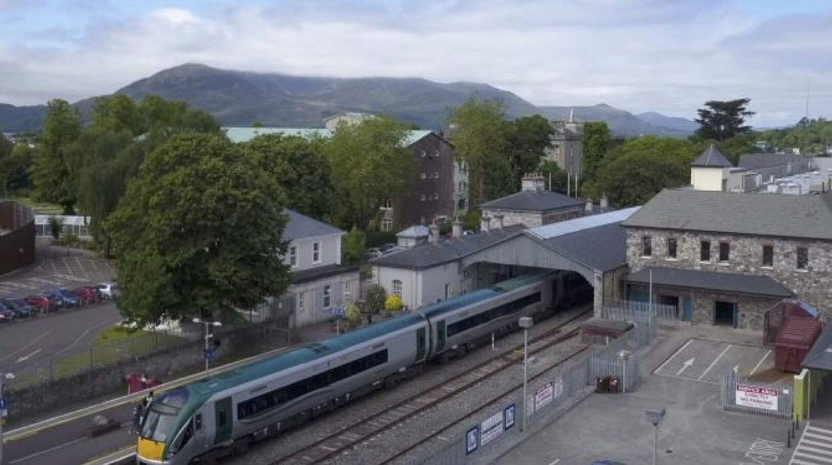 A train station with a modern train, buildings, and a mountainous backdrop.