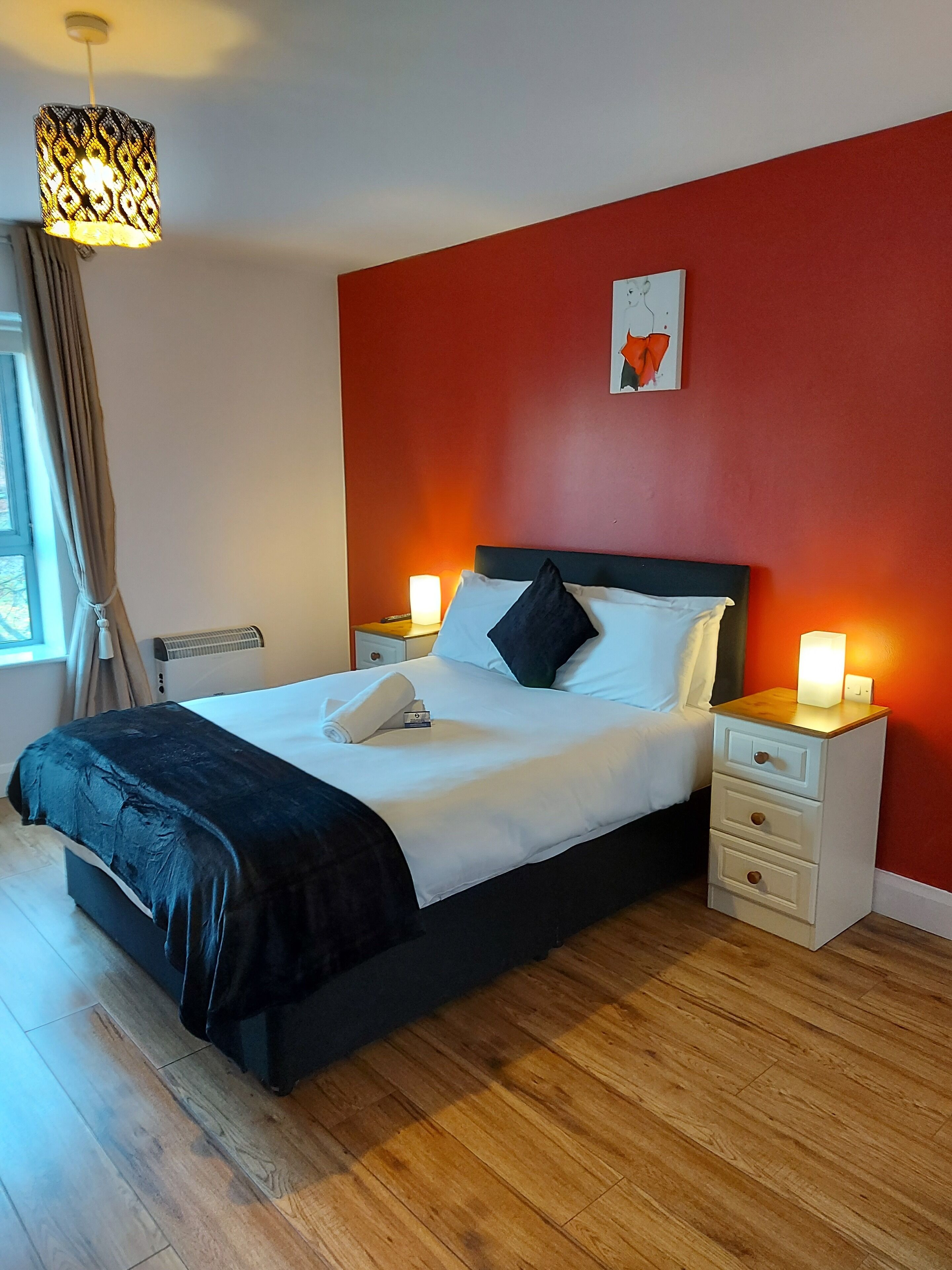 Una habitación de hotel moderna con una cama grande, mesitas de noche y una pared de acento roja.