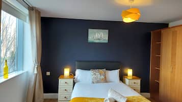 A bedroom with a bed, two bedside tables, a nightstand, a window with curtains, a painting, and a wardrobe.