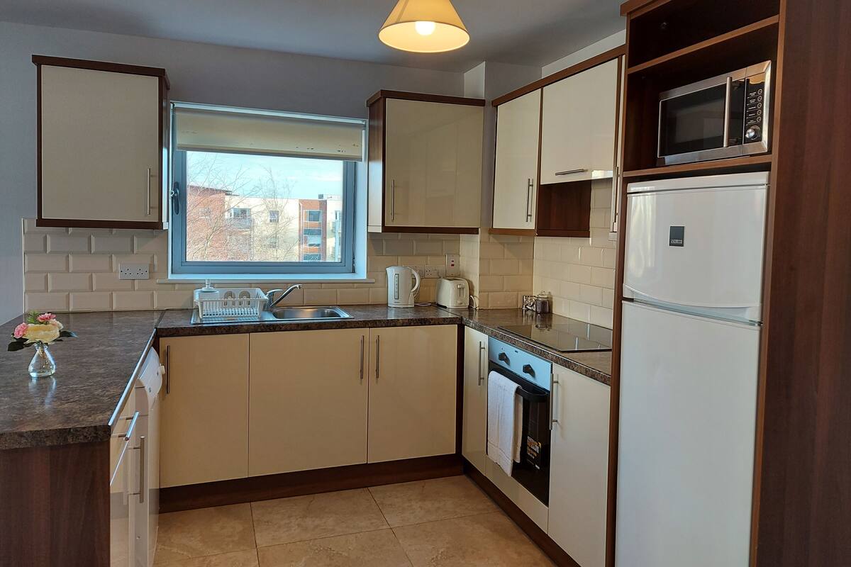 A kitchen with white cabinets, a built-in microwave, a dishwasher, and a window providing natural light.