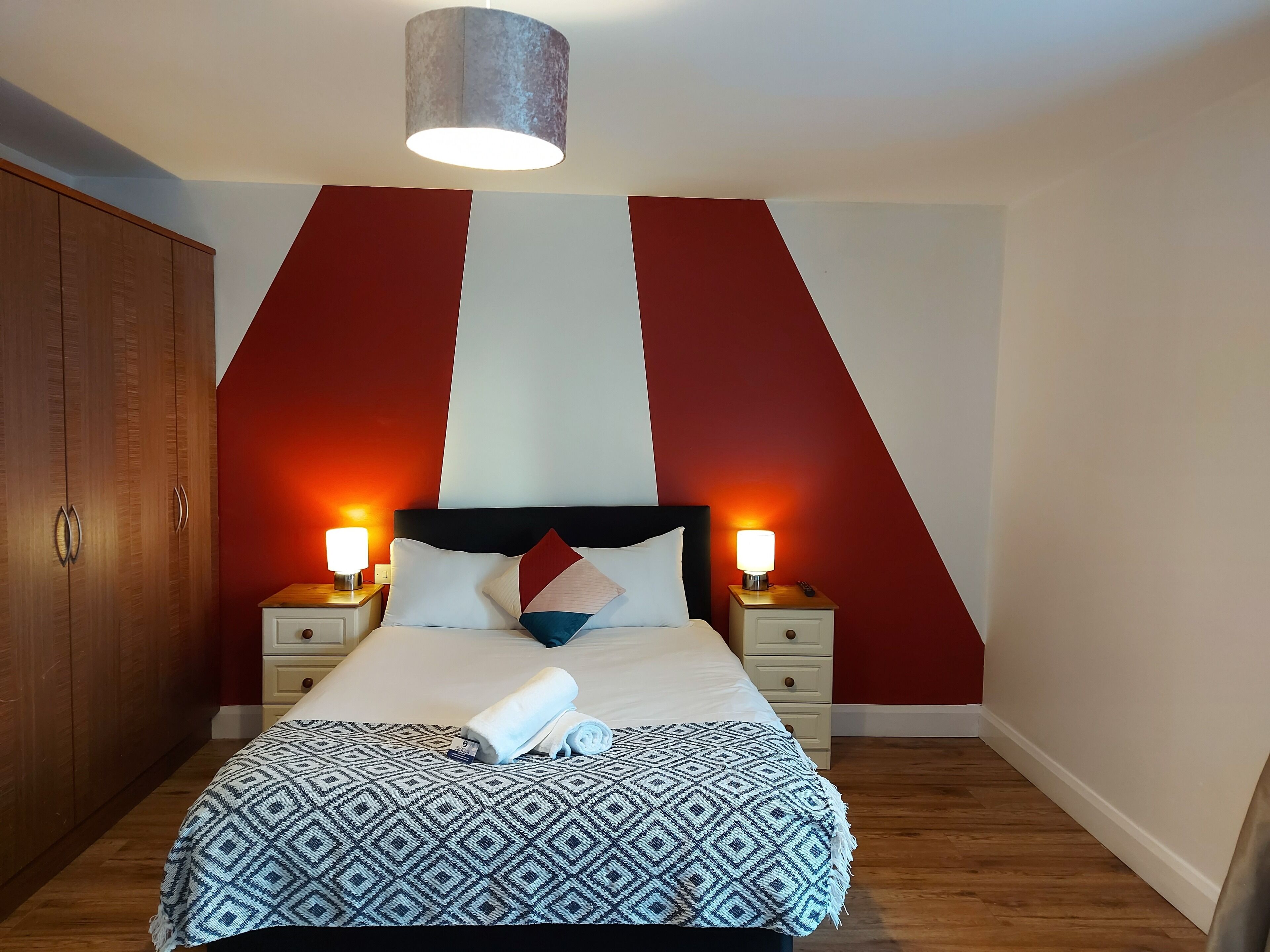 A neatly made bed with a patterned blanket, two bedside lamps, and a wooden wardrobe.