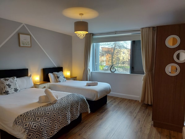 Habitación de hotel con dos camas, un ventanal grande con cortinas, un armario de madera y un candelabro.