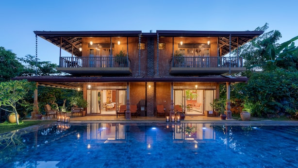 Una casa de dos pisos con piscina delantera, con balcones y mobiliario exterior.