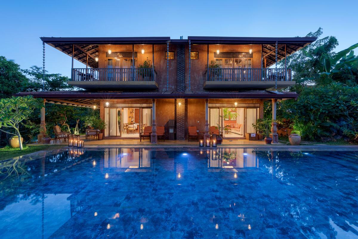 Una casa de dos pisos con piscina delantera, con balcones y mobiliario exterior.