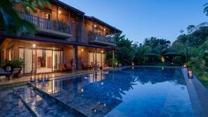 Una casa de dos pisos con piscina, mobiliario exterior y balcón.