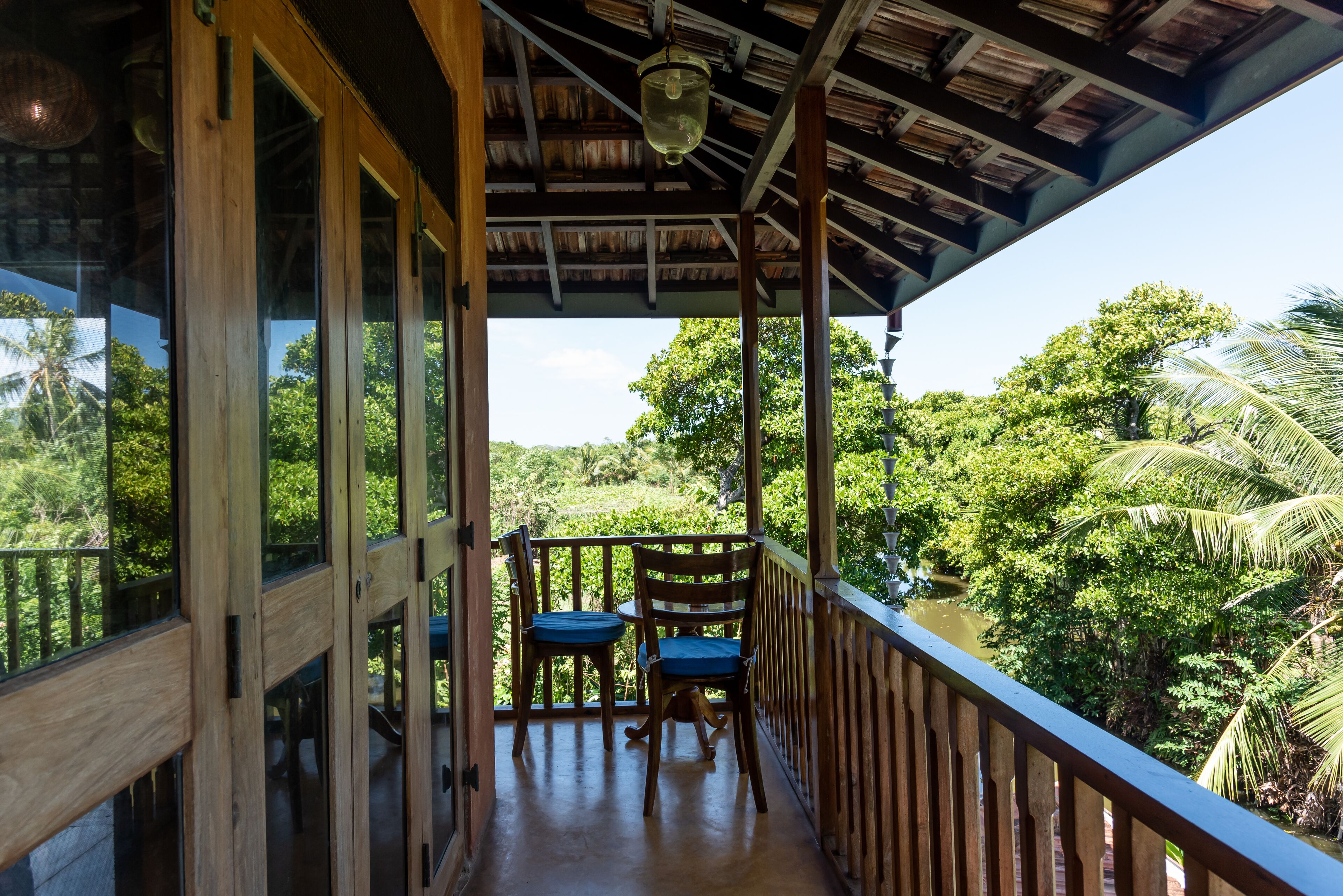 A wooden balcony with two chairs and a table, overlooking a lush green landscape.
