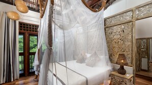 Una habitación con una cama bajo un dosel, una mesita de noche con una lámpara y un panel decorativo en la pared.