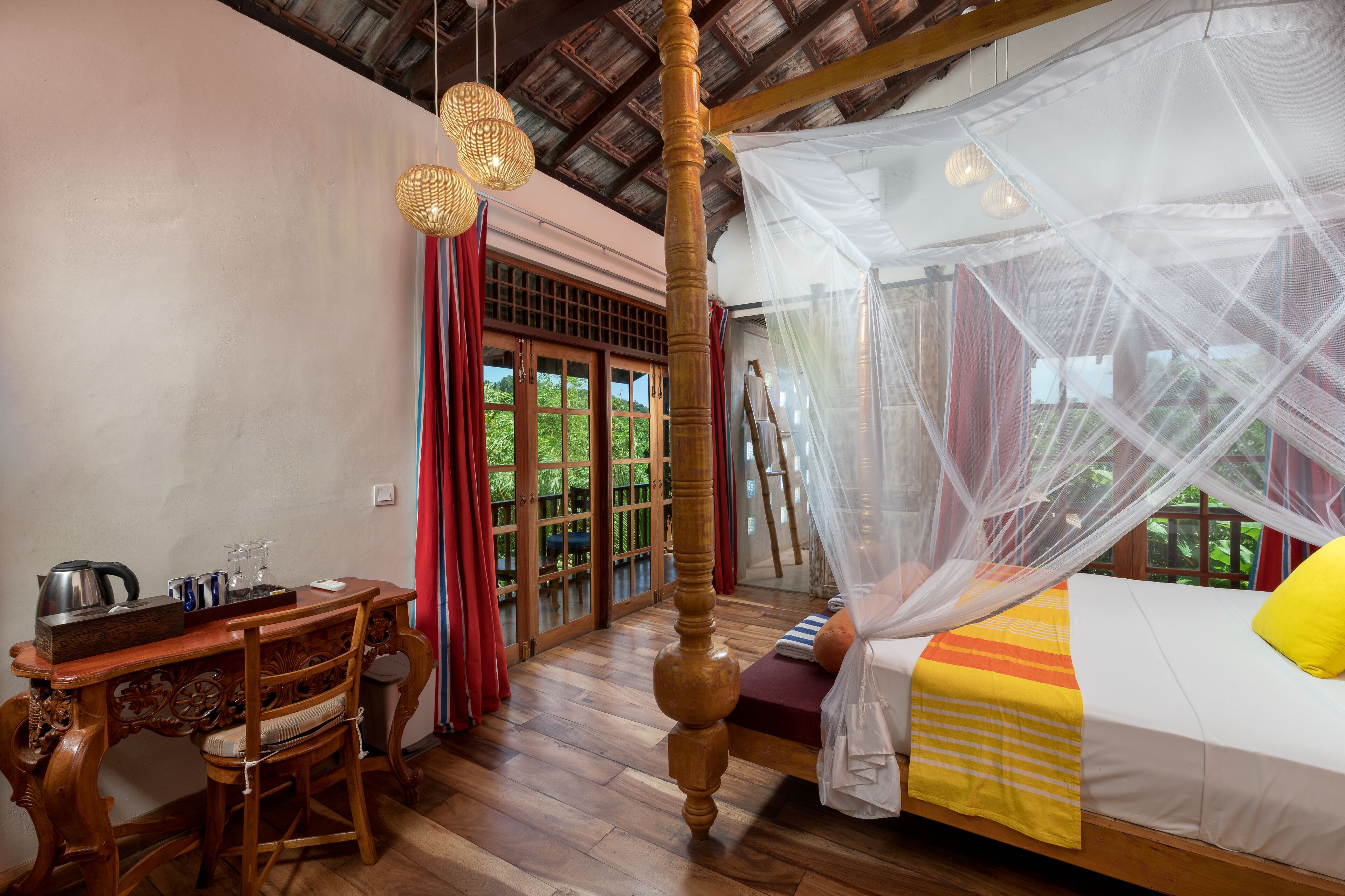 A room with a wooden bed, a desk with a kettle, and a chair.