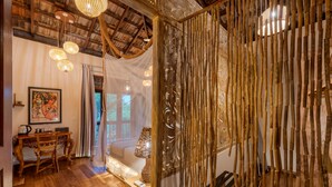 Una habitación con techo de madera, una cama, una mesa con sillas y una pared decorativa de bambú.