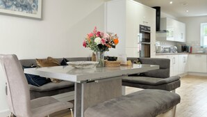 Eine moderne Küche mit weißen Schränken, einem Esstisch mit grau gepolsterten Stühlen und einer Vase mit Blumen auf dem Tisch.