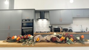 Eine moderne Küche mit grauen Schränken, einer zentralen Kochinsel mit einer dekorativen Herbstkomposition aus Blättern und Kürbissen sowie einem Einbauofen.