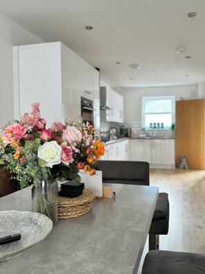 Una cocina moderna con armarios blancos, una mesa de comedor con un jarrón de flores y un control remoto sobre la mesa.
