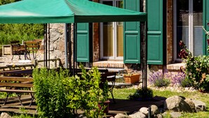 Un patio con mobiliario exterior, una sombrilla verde y un edificio de ladrillo con contraventanas verdes.
