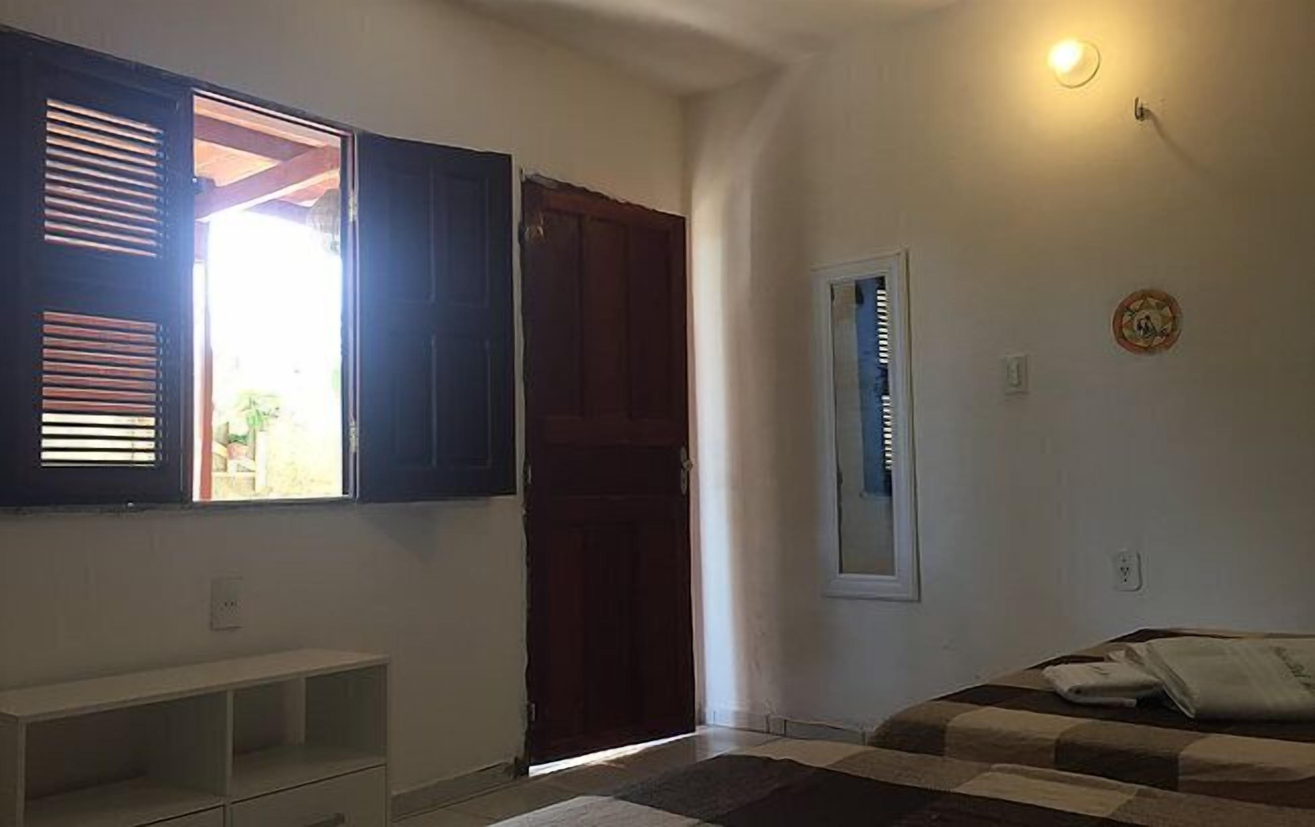 A bedroom with a bed, a wardrobe, a window with blinds, and a wall-mounted light fixture.